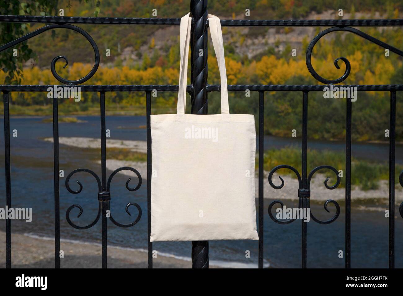 Canvas tote bag hanging on the park fence mockup. Rustic linen shopper bag mock up for branding presentation Stock Photo