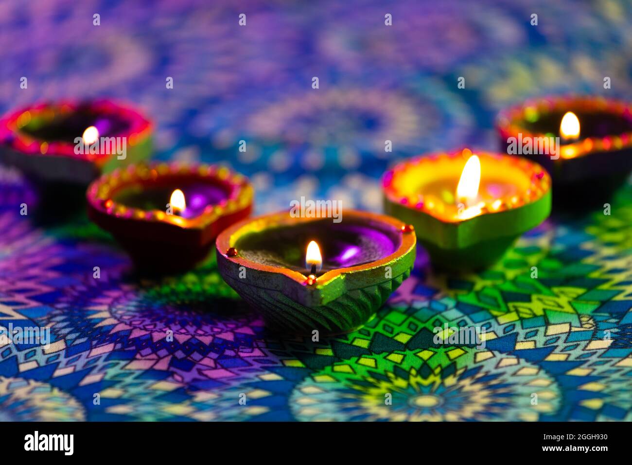 Lit candles in small decorative clay pots burning on patterned table cloth Stock Photo