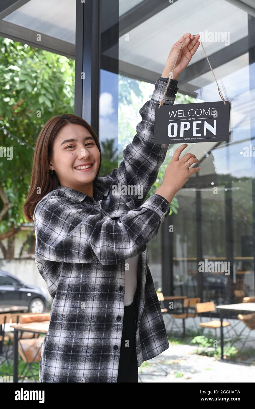 Smiling Asian woman turning open sign broad on the door glass and ready to service. Stock Photo