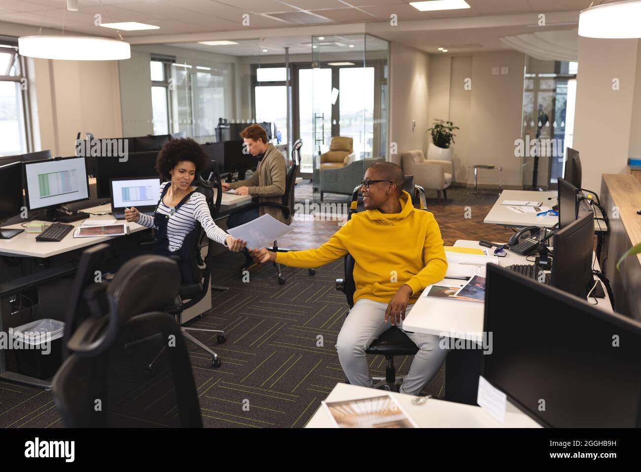 Diverse male and female colleagues at work, sitting at desks, using ...