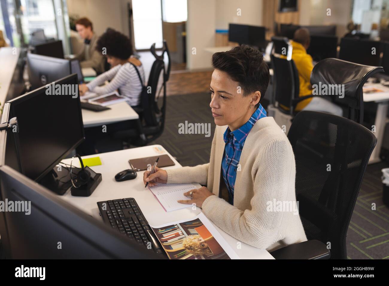 Mixed race female creative at work, sitting at desk, using computer Stock Photo