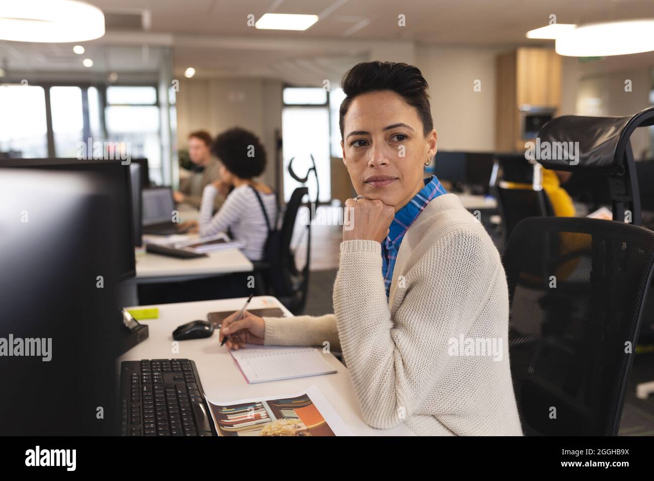 Mixed race female creative at work, sitting at desk, using computer Stock Photo