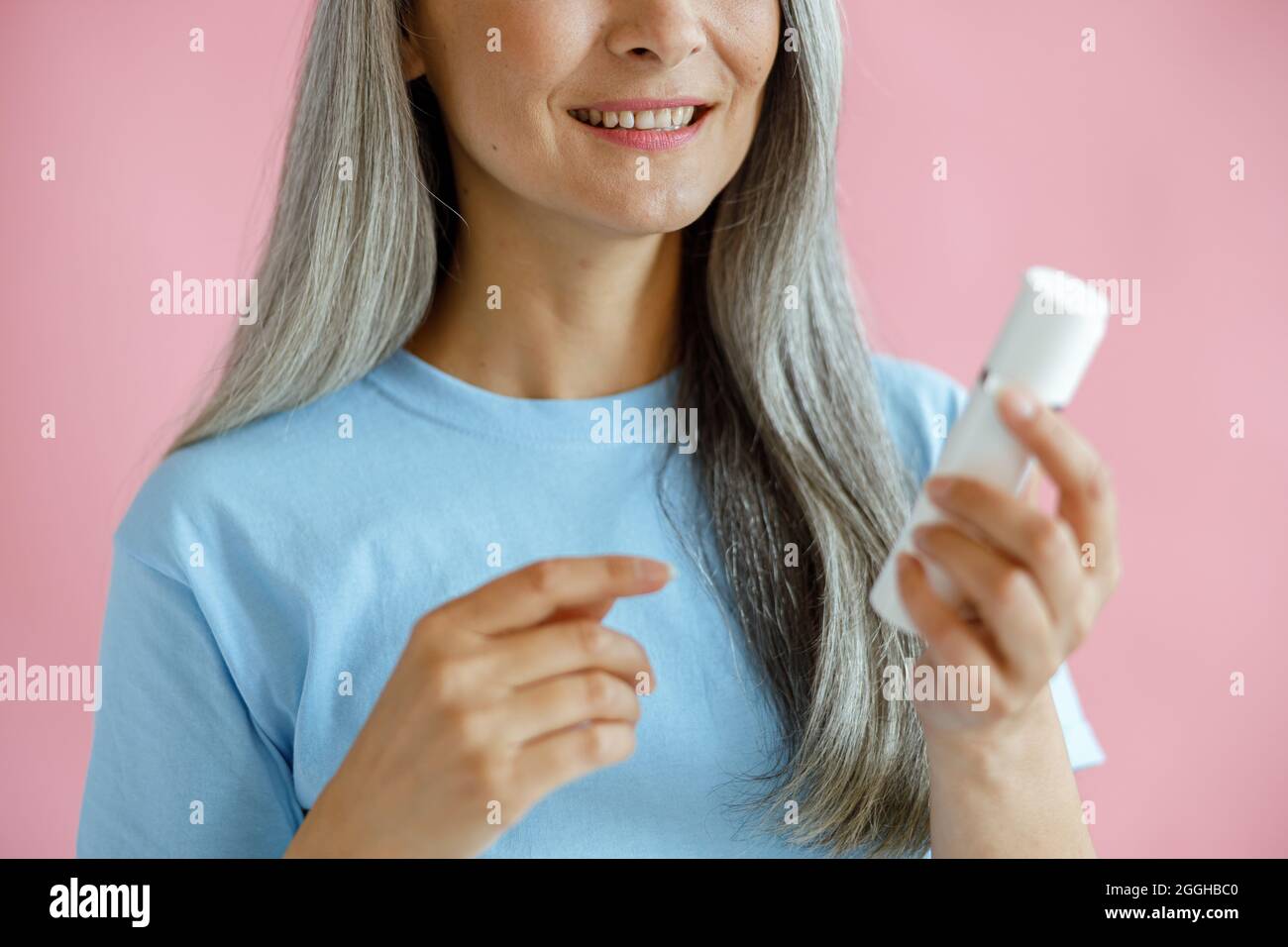 Smiling mature grey haired Asian lady holds bottle of cosmetic product in studio Stock Photo