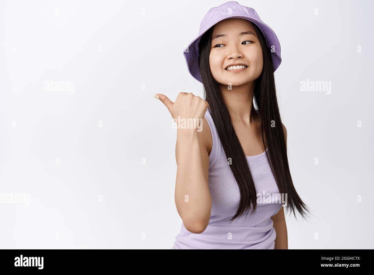 Beautiful asian girl pointing finger left, looking happy behind her ...