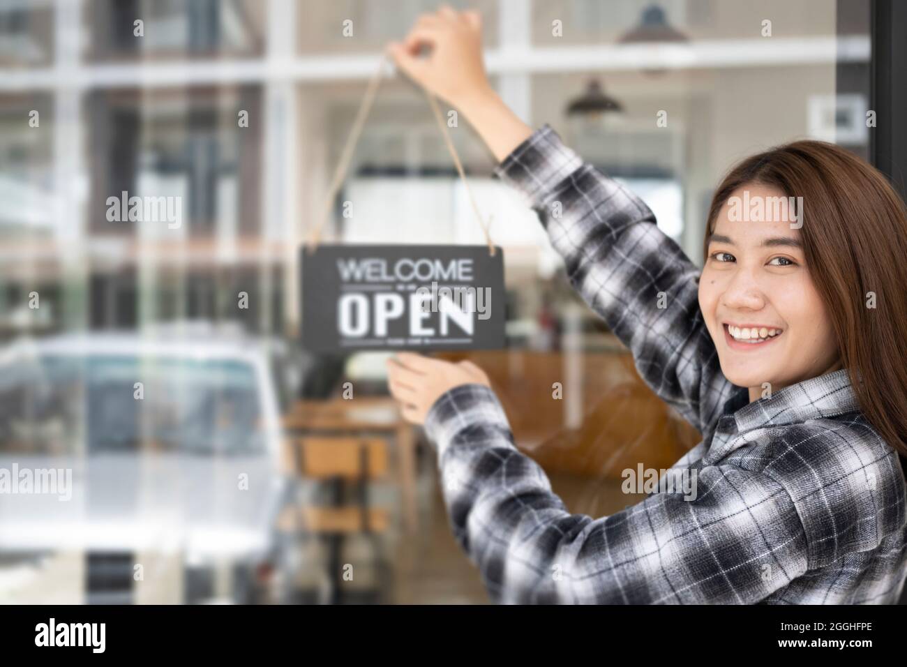 Small business owner turning open sign board on glass window. Stock Photo