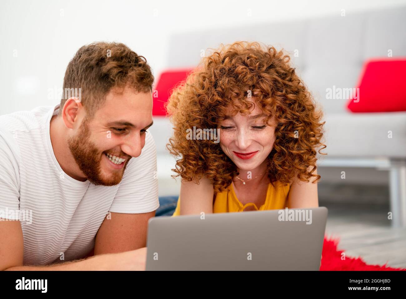 A Young couple lovers or friends laying on a red pluffy carpet and using laptop. High quality photo Stock Photo