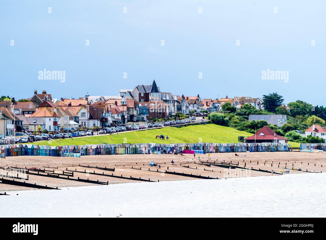 View along the shingle beach with groynes, and the residential part of the town. Dark rain clouds over the town, with white and blue sky over the sea. Stock Photo