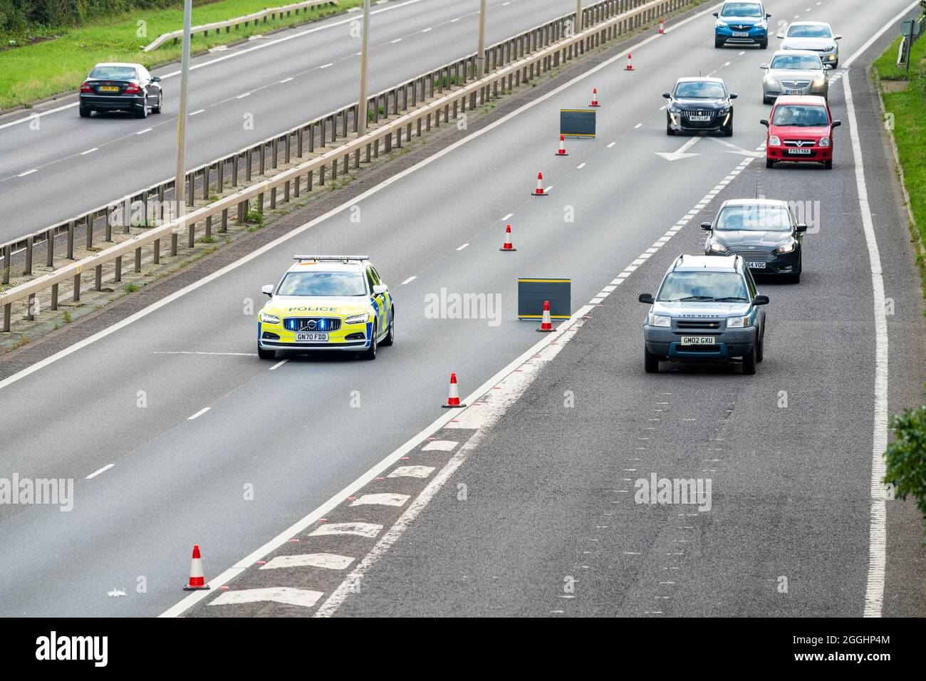 Police car on main road, A299, behind traffic cones and two signs to block the road off and cars using slip road to follow diversion after incident. Stock Photo