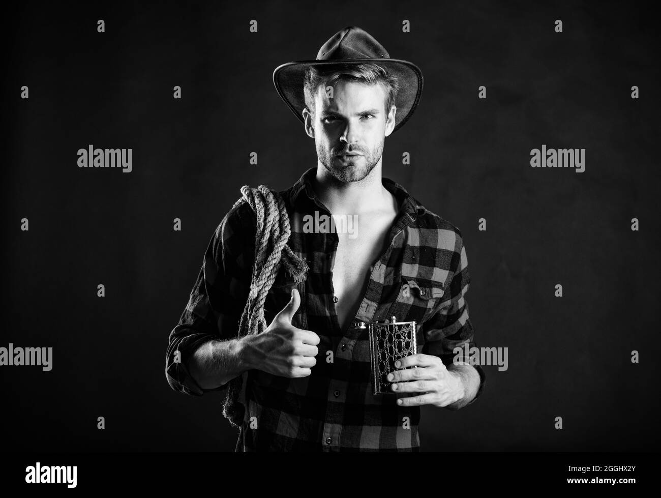 Western culture. Western life. Man wearing hat hold rope and flask. Lasso tool of American cowboy. Man handsome unshaven cowboy black background Stock Photo