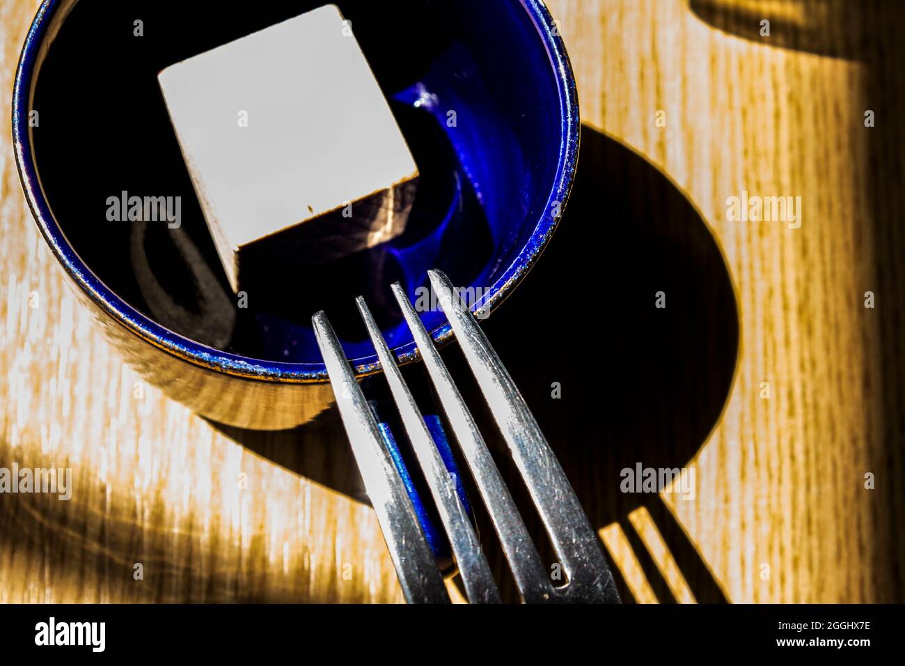 Abstract composition with a fork, a cup, a cube and a wooden table. Stock Photo