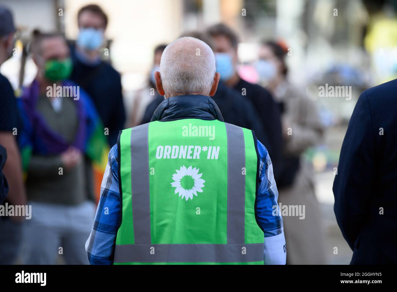 Cottbus, Germany. 01st Sep, 2021. A helper at the election campaign event  of Bündnis 90/Die Grünen on Oberkirchplatz wears a green high-visibility  vest with the gender-appropriate inscription "Ordner*in" ("Steward") during  the event.