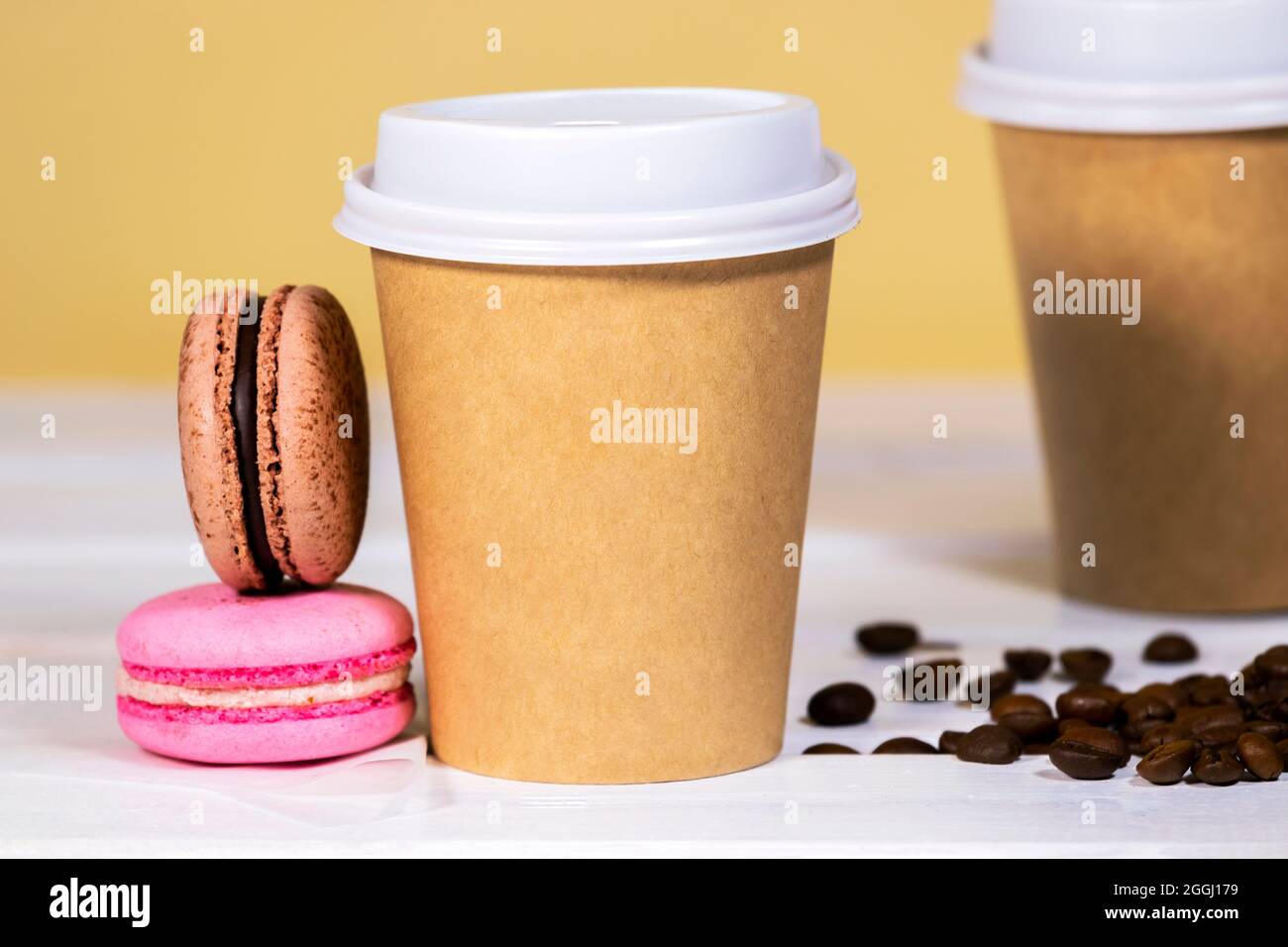Coffee to go in paper eco cup with chocolate french macaroon on wooden and light orange