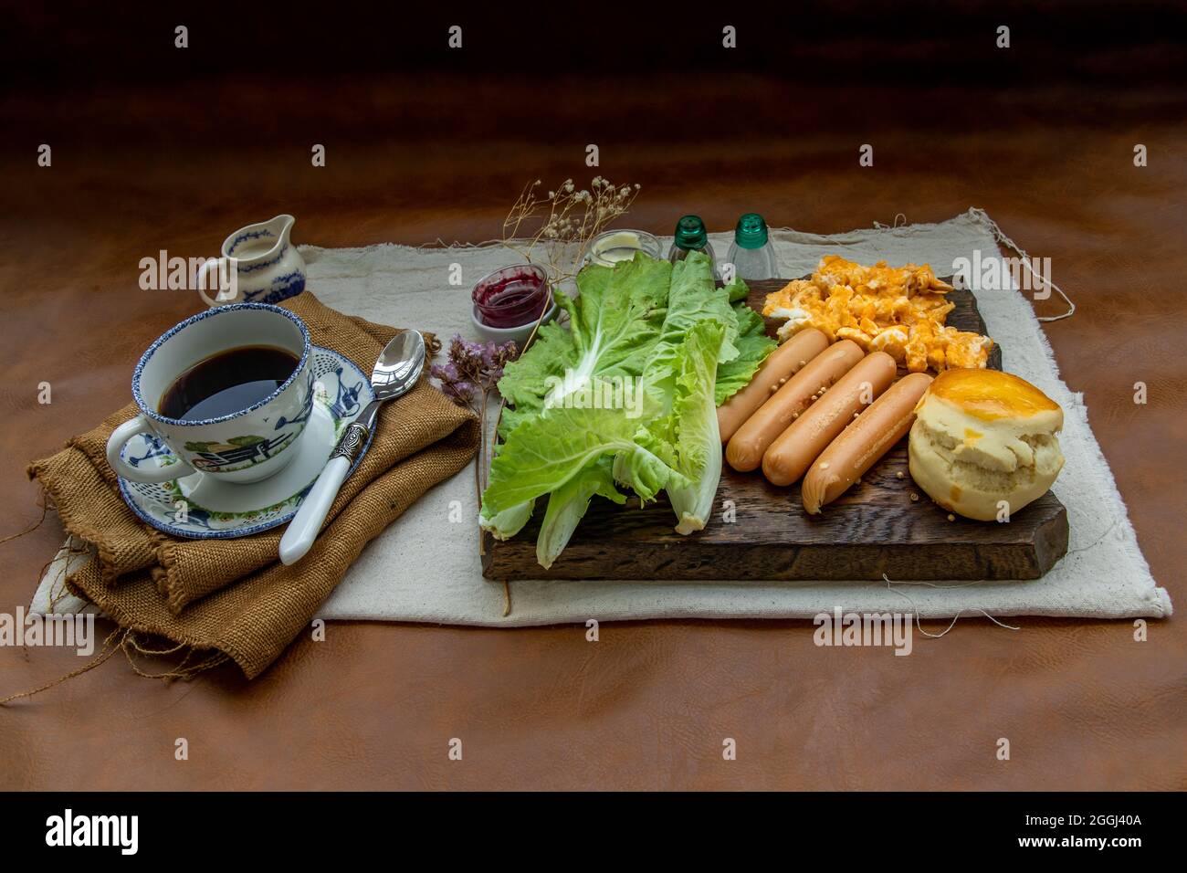 Continental breakfast with scrambled eggs, fried sausages, vegetable and scones served with coffee with milk. Wood background, Selective focuse. Stock Photo
