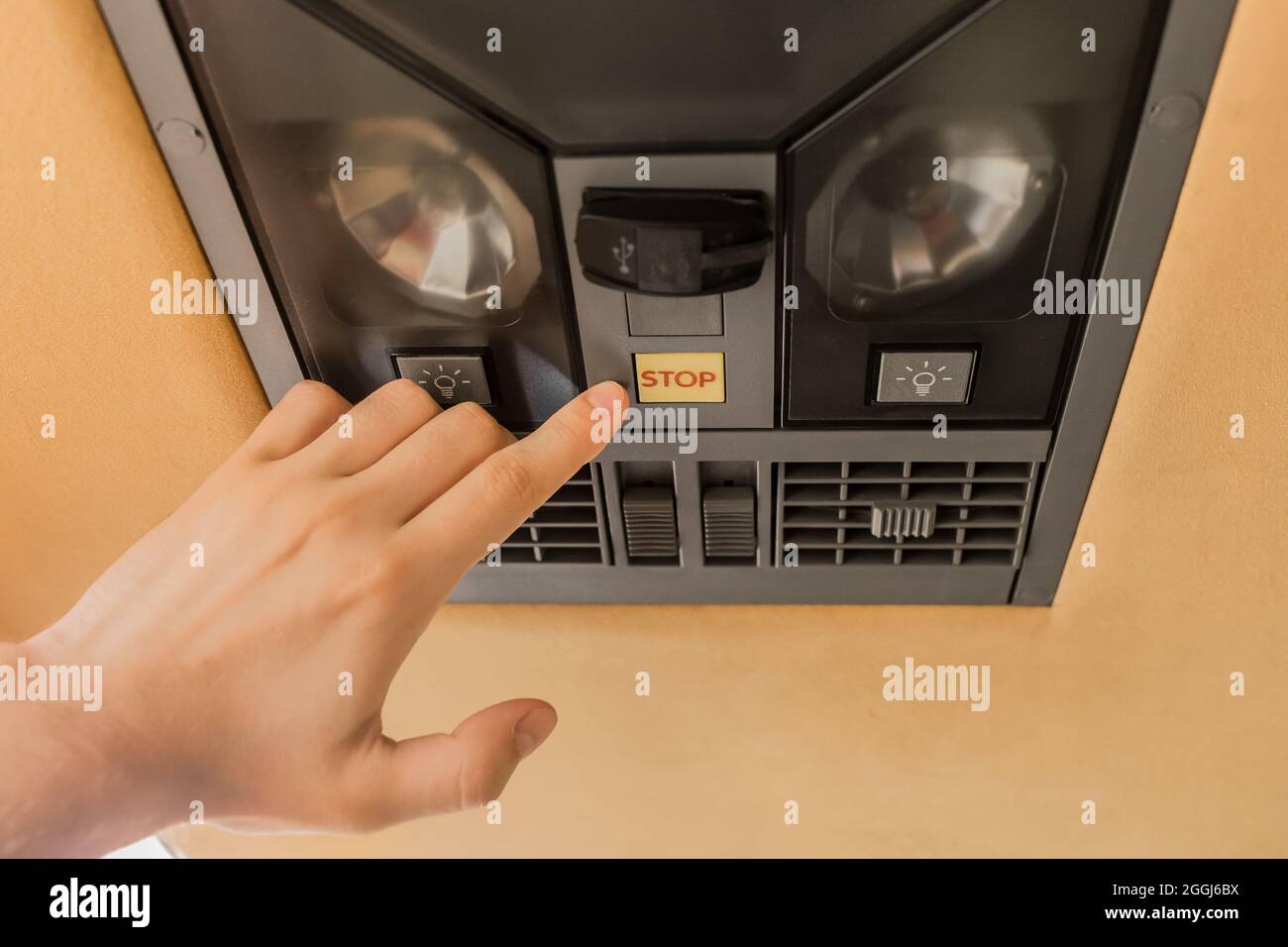 The guy's hand points his finger at the stop button of the air conditioning system in the ceiling of the tourist bus. Stock Photo