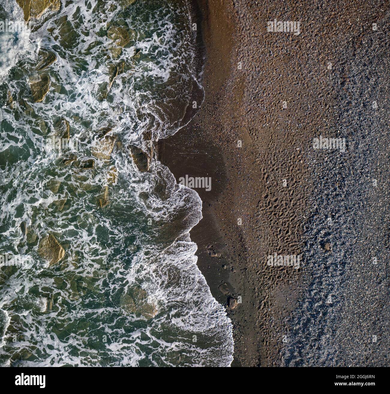 Green waves with white sea foam over dark sandy shore of chocolate color, top view texture Stock Photo