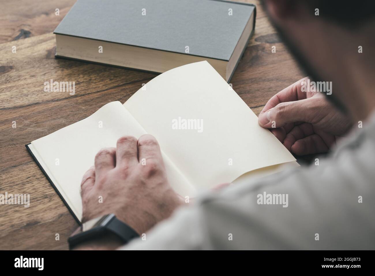 over the shoulder view of person sitting an wooden table reading a book Stock Photo