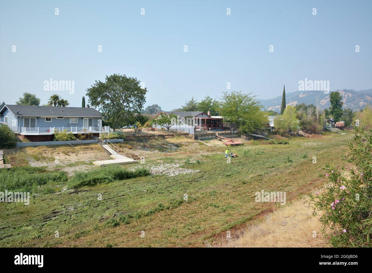 man cutting weeds in dry dried canal behind his home an dock after 8 year drought in northern California fishing lake has no water for  boats acces Stock Photo