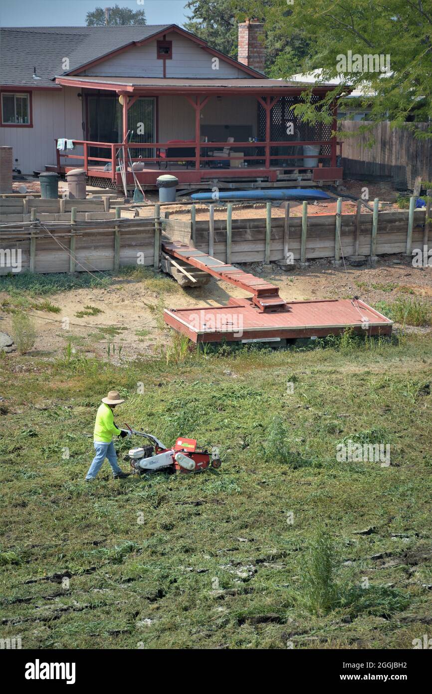 man cutting weeds in dry dried canal behind his home an dock after 8 year drought in northern California fishing lake has no water for  boats acces Stock Photo