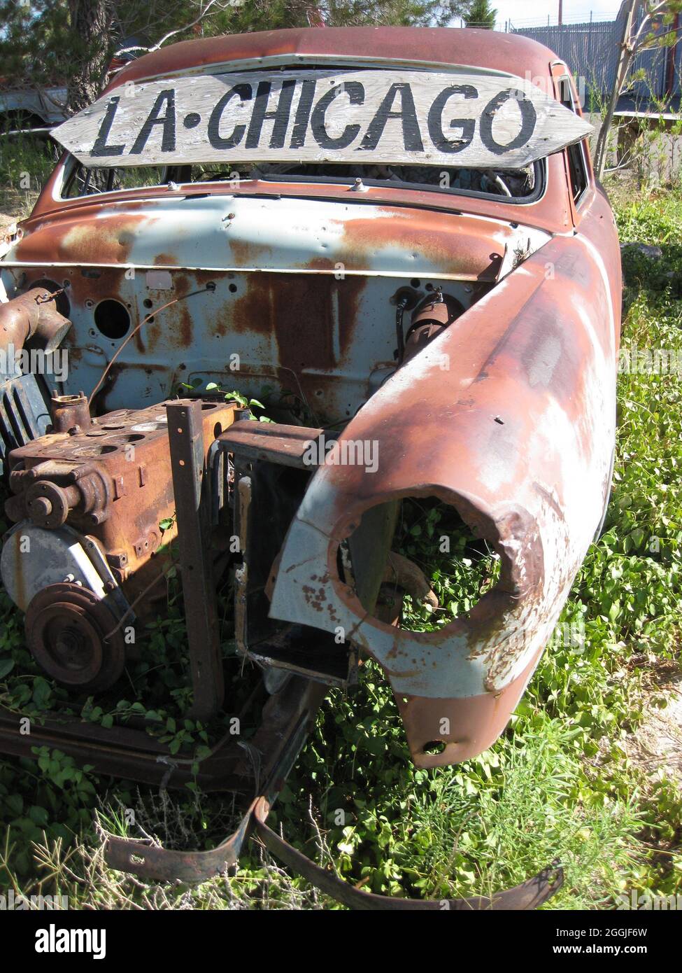 An old rusted-out vintage car covered in overgrowth with a sign saying LA - Chicago Stock Photo