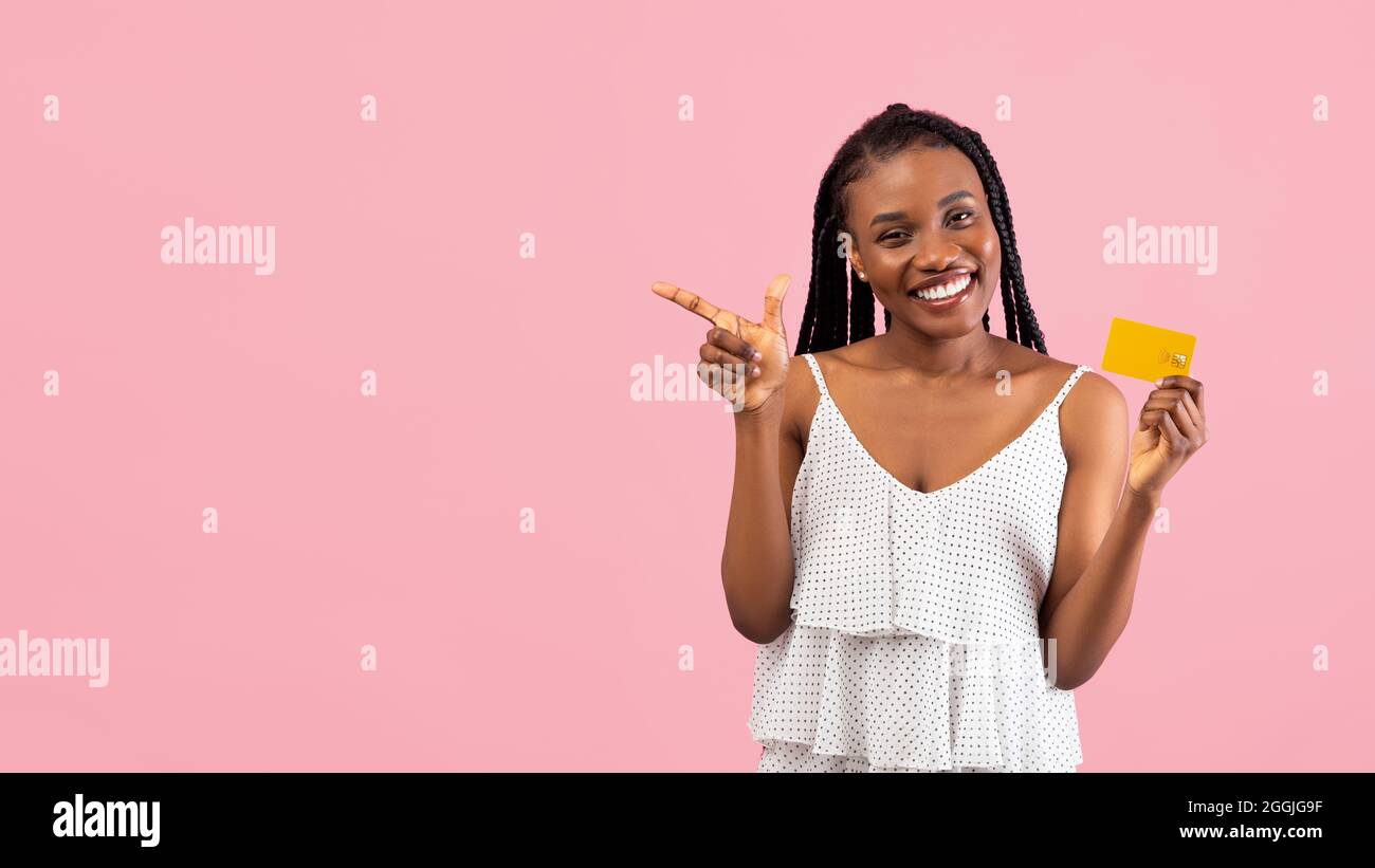 Positive black lady showing credit card, pointing aside at blank space ...