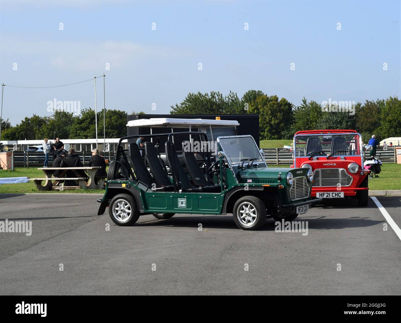 Two new mini mokes 2021 one red and one green with people in the background Stock Photo