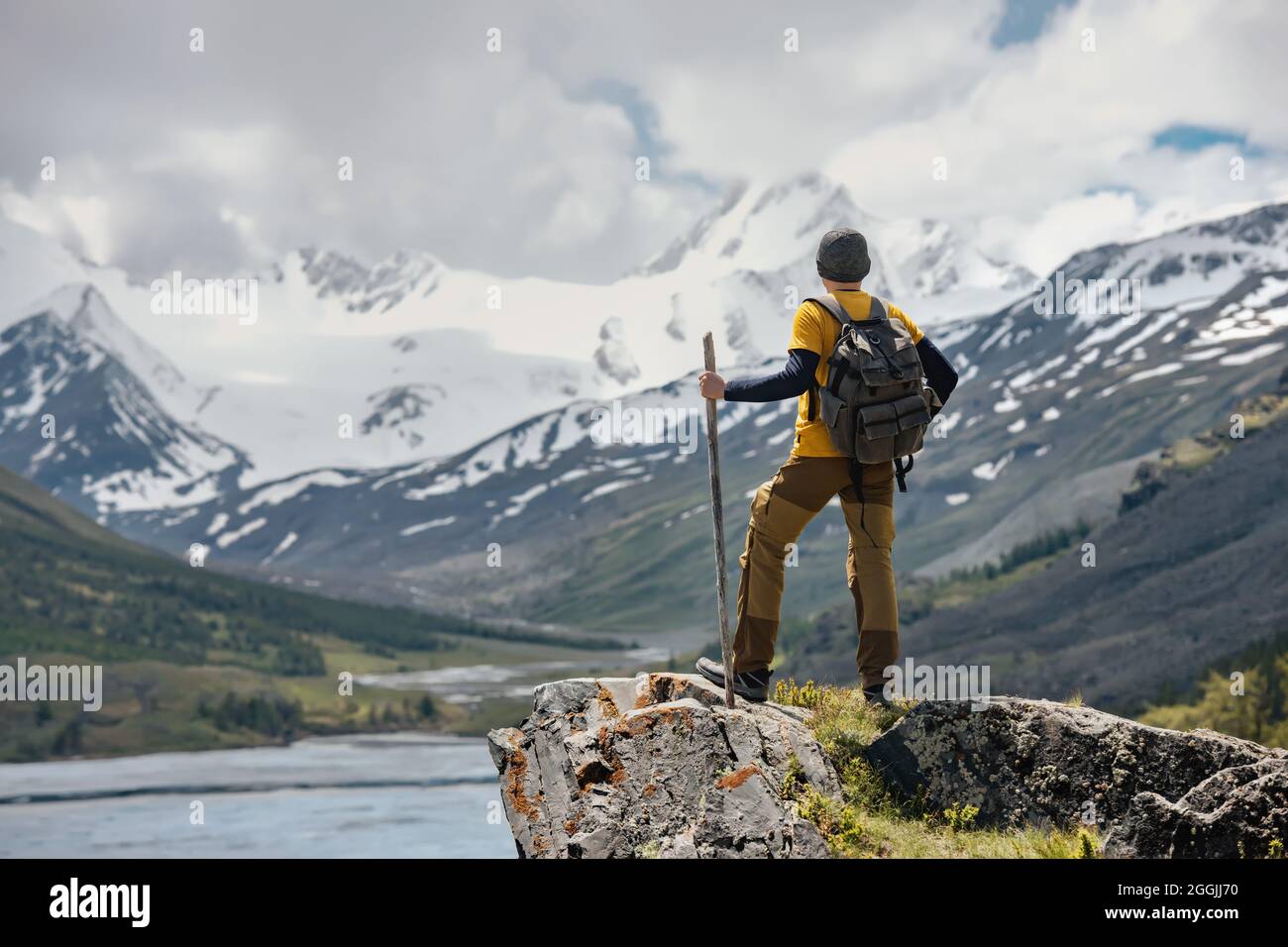 Traveler or backpacker stands with backpack on big rock and looks at glacier and river Stock Photo