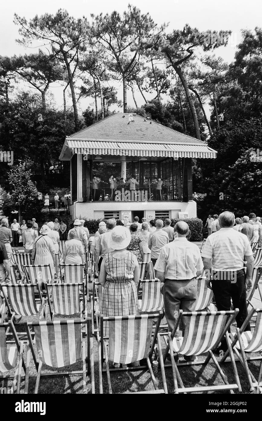 An elderly audience stand up from their deckchairs for the playing of the National Anthem at a concert in Pine Walk Bandstand, Lower Gardens, Bournemouth, Dorset, England, UK. Circa 1980's Stock Photo