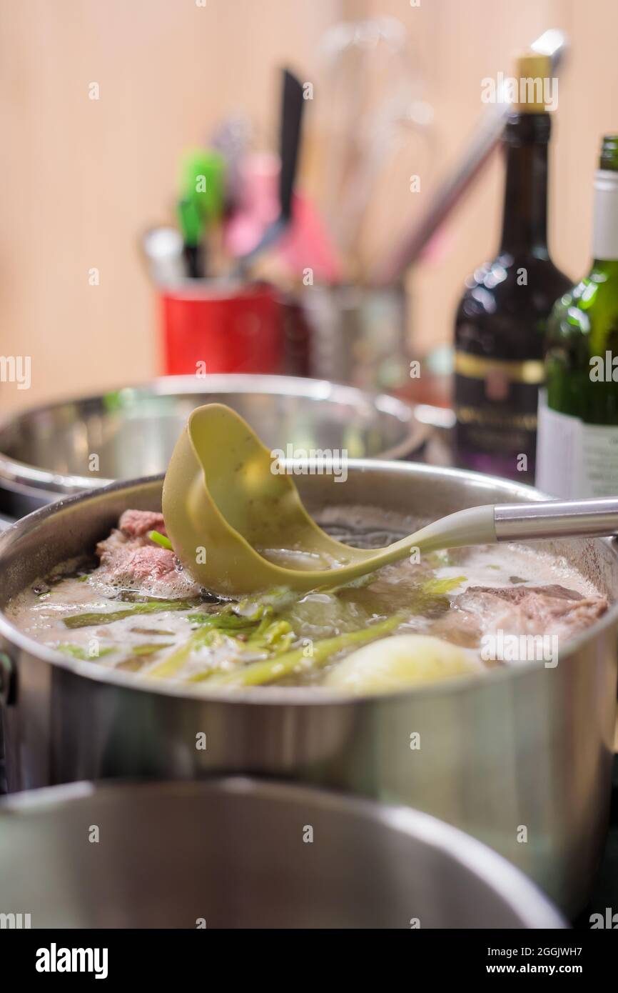A metal saucepan filled with boiling vegetable and meat broth. There is a scoop in the broth. Close-up. Stock Photo