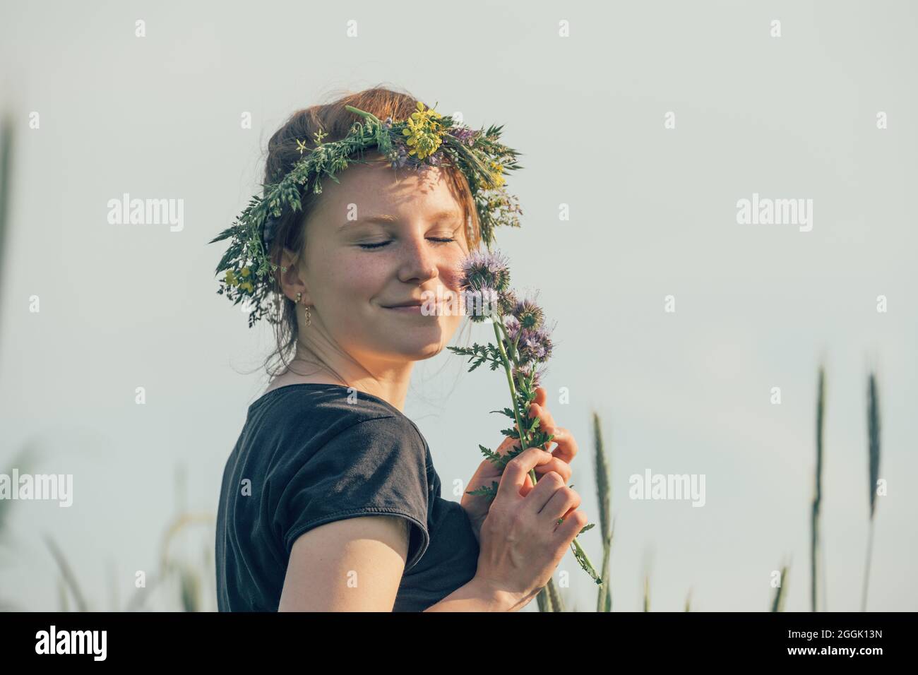 Young woman with wreath of natural flowers on her head, dreamy, holds flowers in her hand Stock Photo