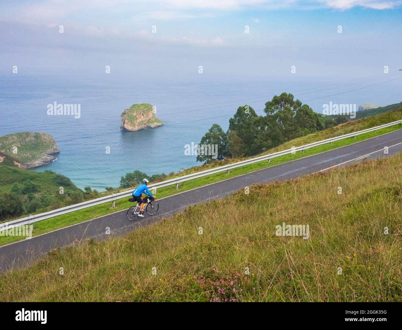 Road bike tour with luggage, bikepacking on a lonely coastal road in Asturias, Northern Spain with a view of the Atlantic Ocean and the beach of Playa de la Ballota near Llanes in Asturias Stock Photo