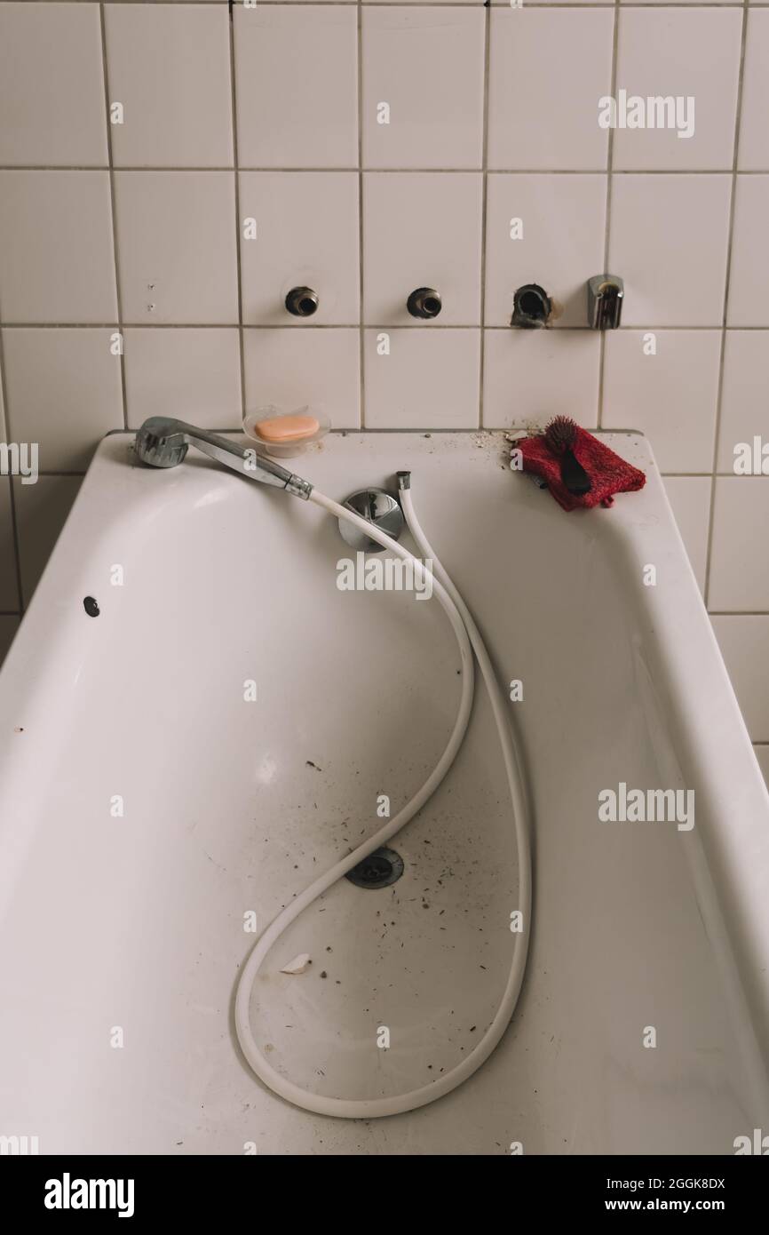 Close up of a broken and old white bath tub with white tiled floor in