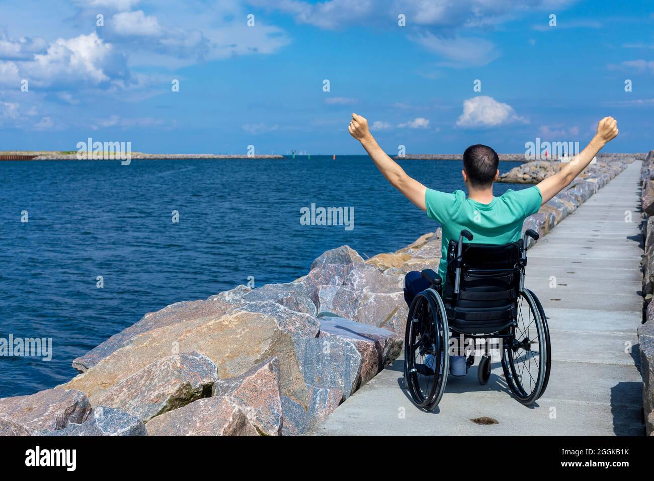 Disabled man in a wheelchair admiring the sea. Travel, mobility and freedom concept. Stock Photo
