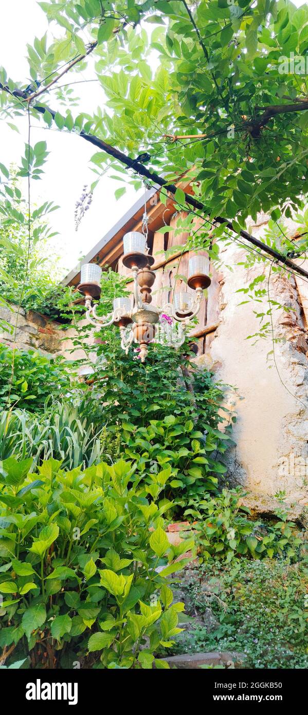 Chandelier hangs between green plants in the garden, Italy, Lombardy, Region Idrosee Stock Photo