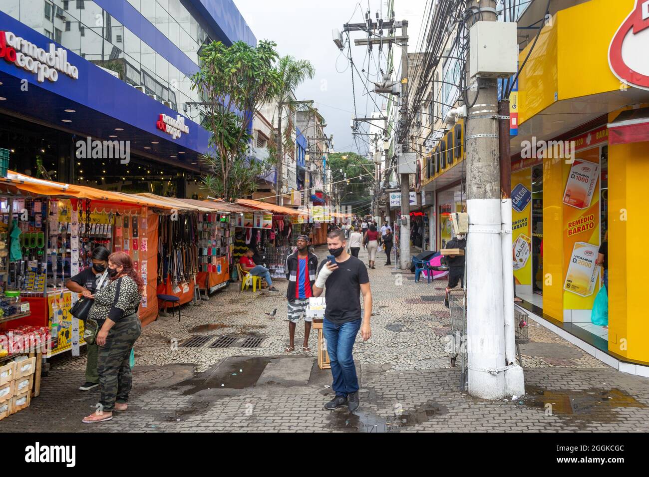 People out and about a narrow cobblestone street where a market is set in Niteroi, Rio de Janeiro, Brazil. A line up of market stalls are seen to the Stock Photo