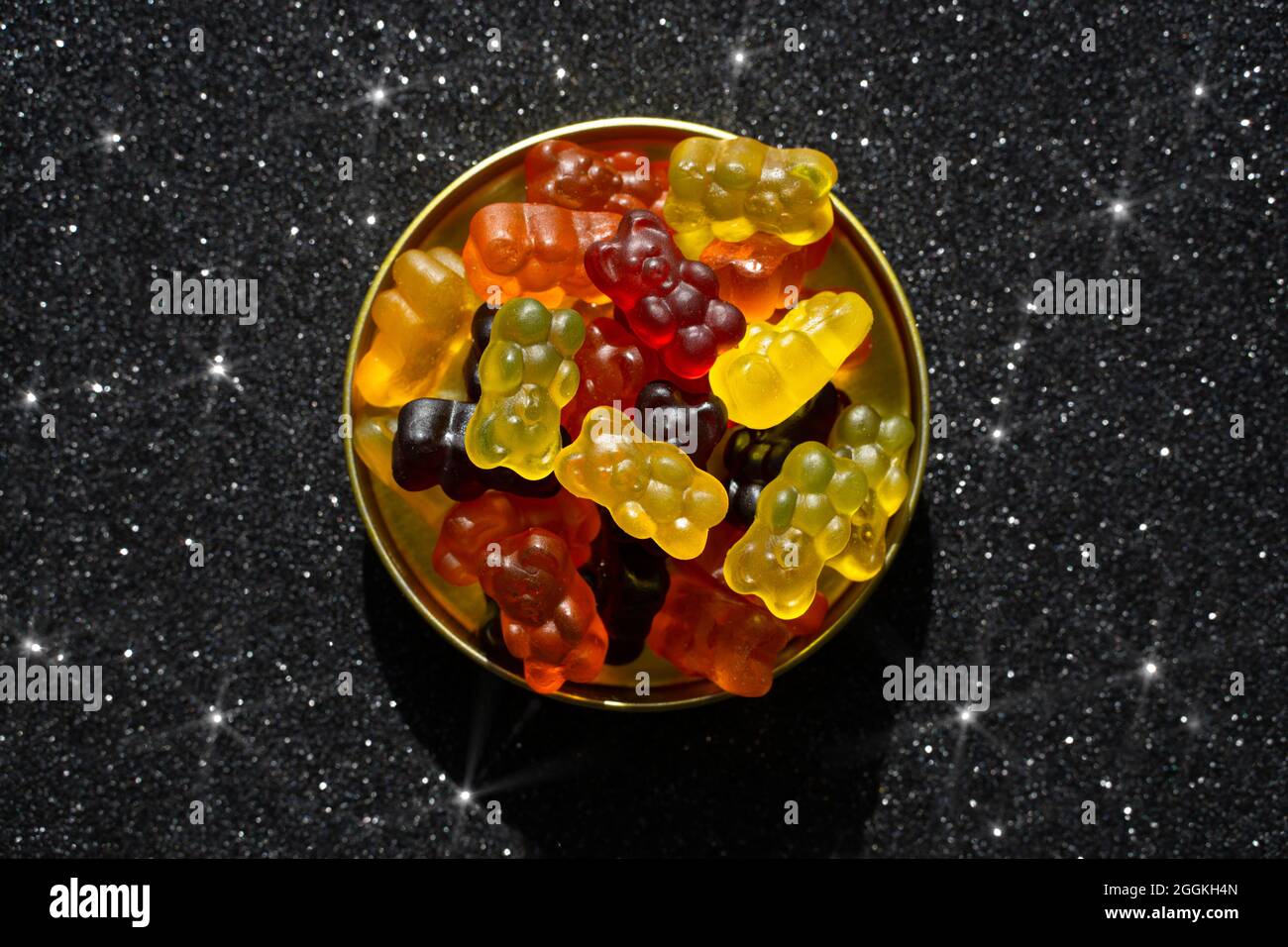 Assortment of gummy bears in a round ting box on a glittering black background Stock Photo