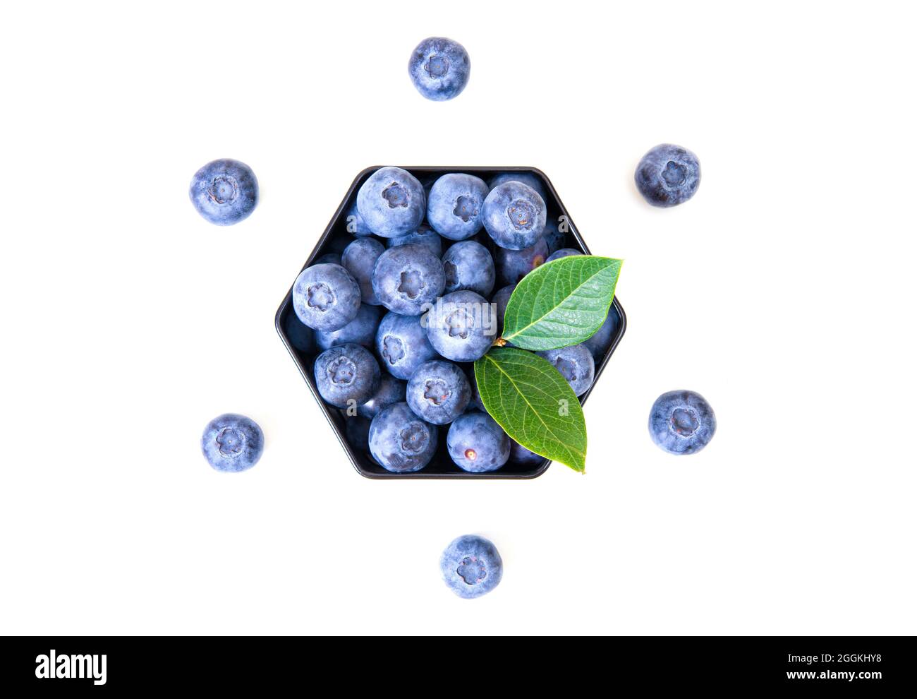 Blueberries in a hexagon box with green leaves on top isolated on white. Creative dessert composition. Stock Photo