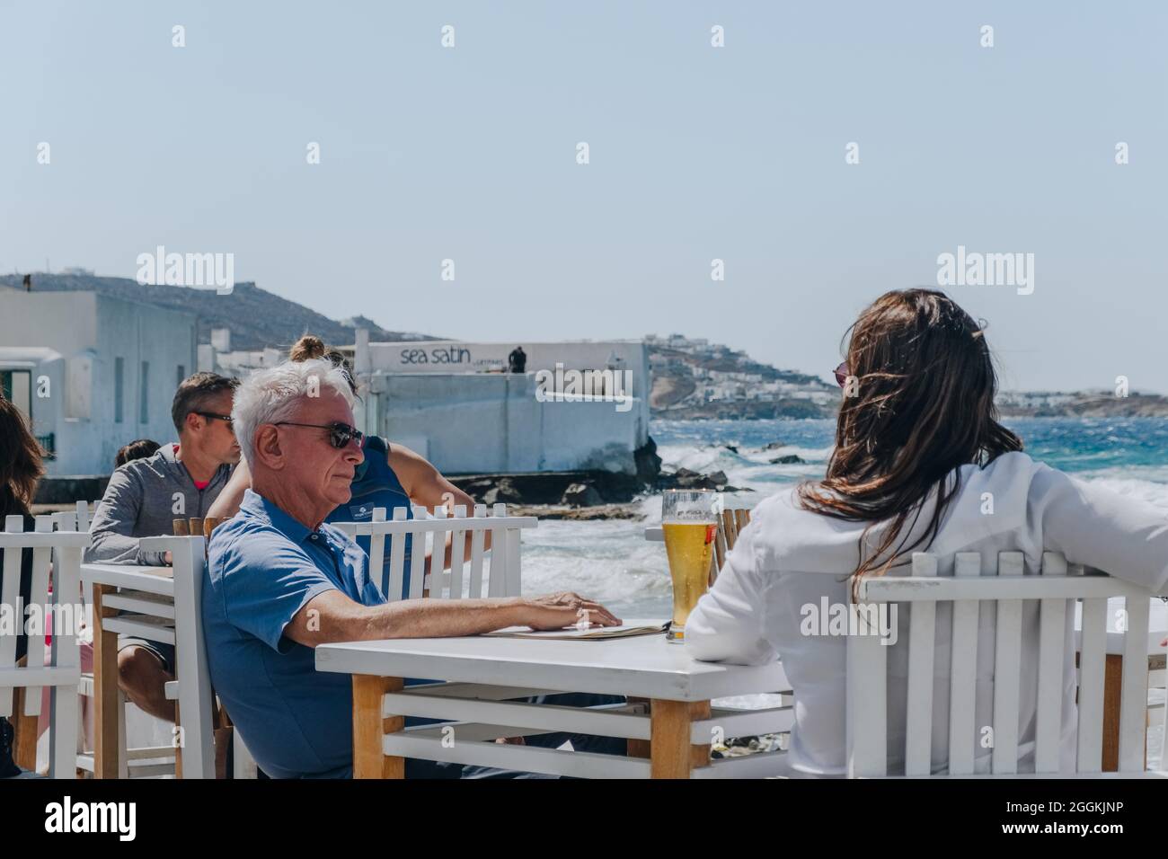 Mykonos Town, Greece - September 24, 2019: Middle aged couple relaxing at the outdoor tables of a restaurant by the water in Hora (also known as Mykon Stock Photo