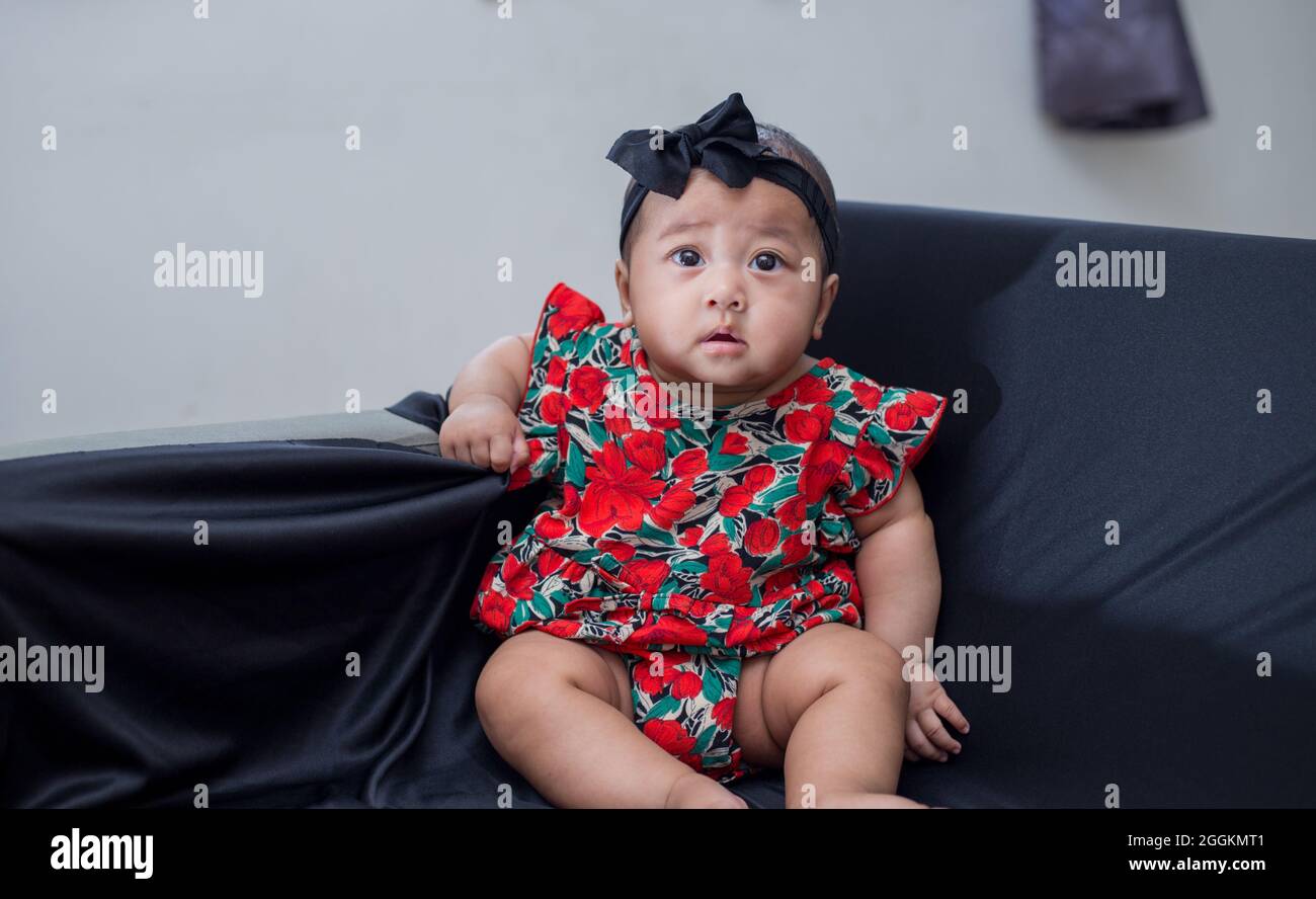 Adorable Toddler Girl From Malaysia In A Beautiful Floral Dress And A Headband Sitting On A Sofa Stock Photo Alamy