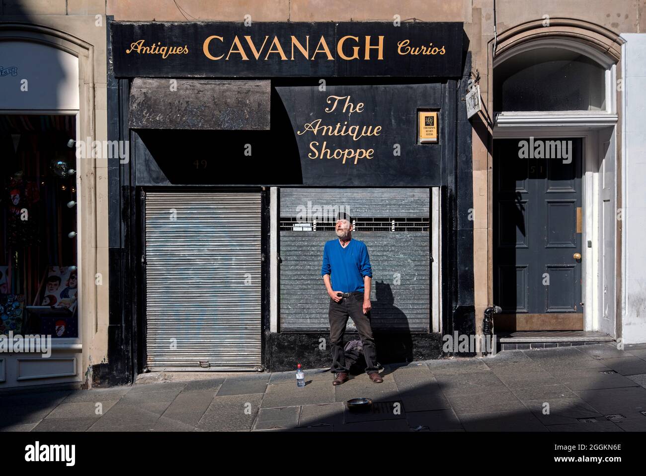 A busker singing Irish and Scottish ballads outside a shuttered antique shop in Cockburn Street in Edinburgh's Old Town. Stock Photo