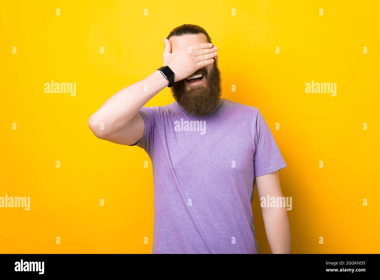 Smiling happy man is covering his eyes with his hand over yellow ...