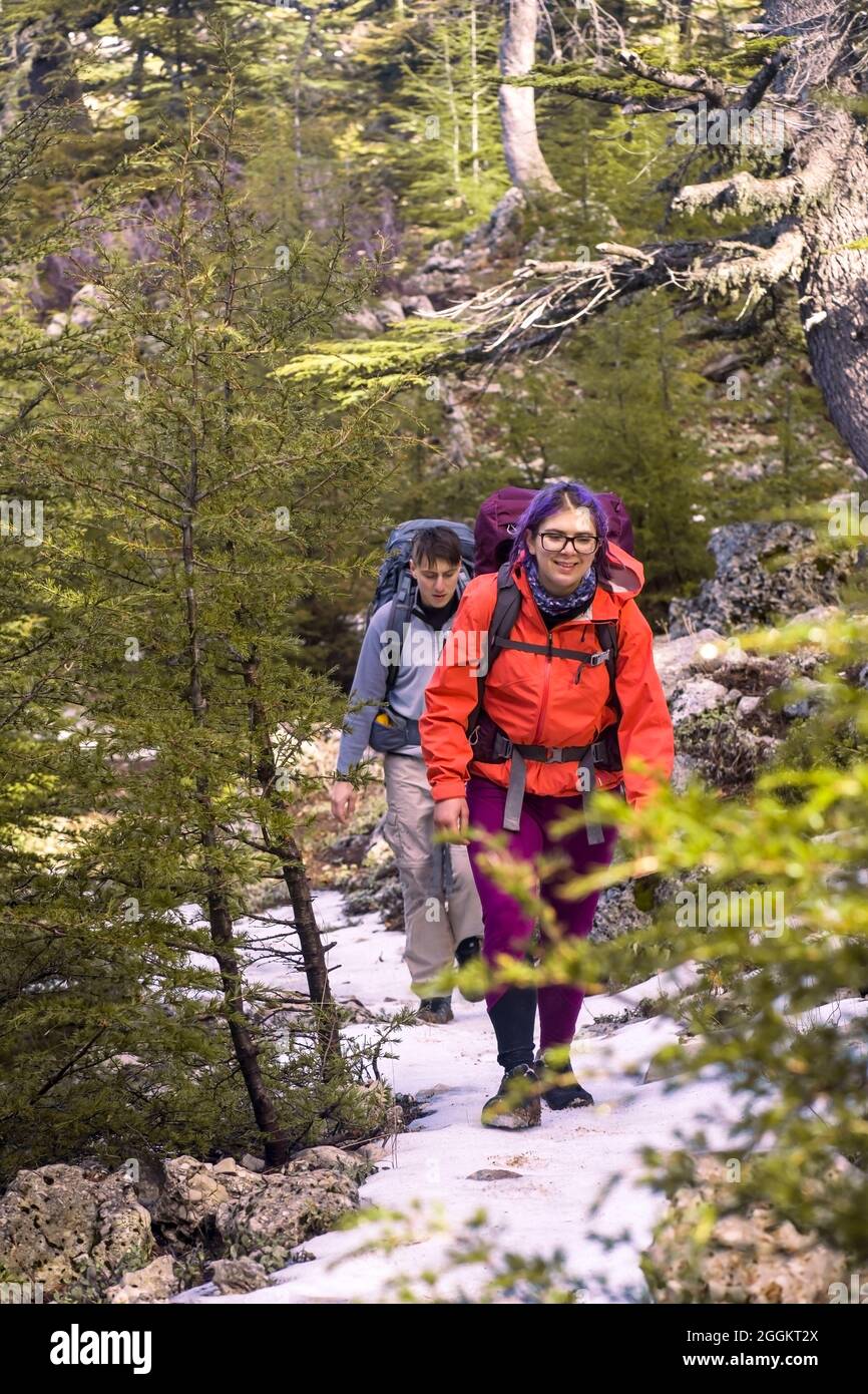 Two young travelers with backpacks are walking along a mountain Stock Photo