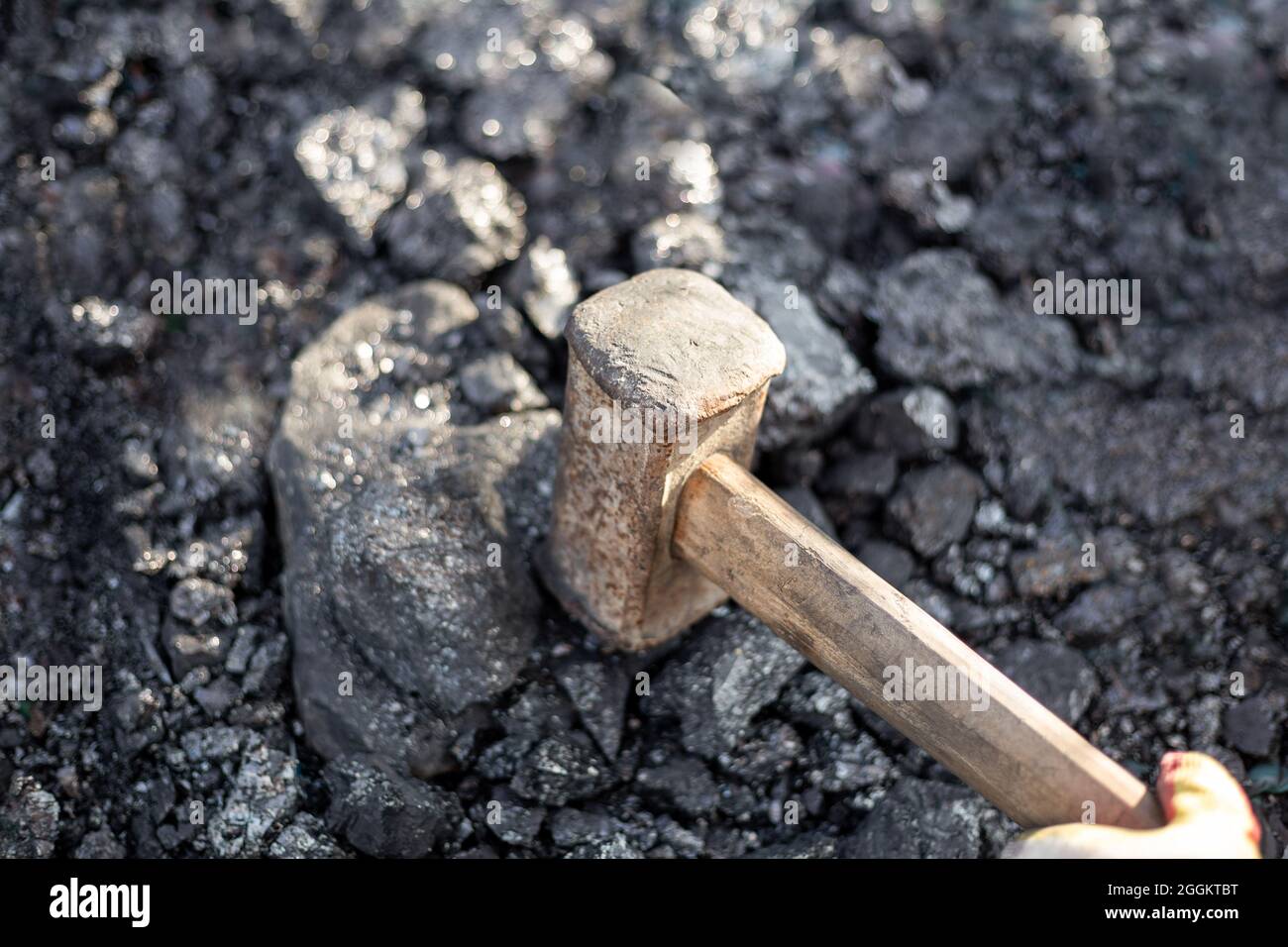 A man smashes large pieces of coal with a sledgehammer. Mineral solid fuel for stoves and fireplaces in the cool season. Stock Photo