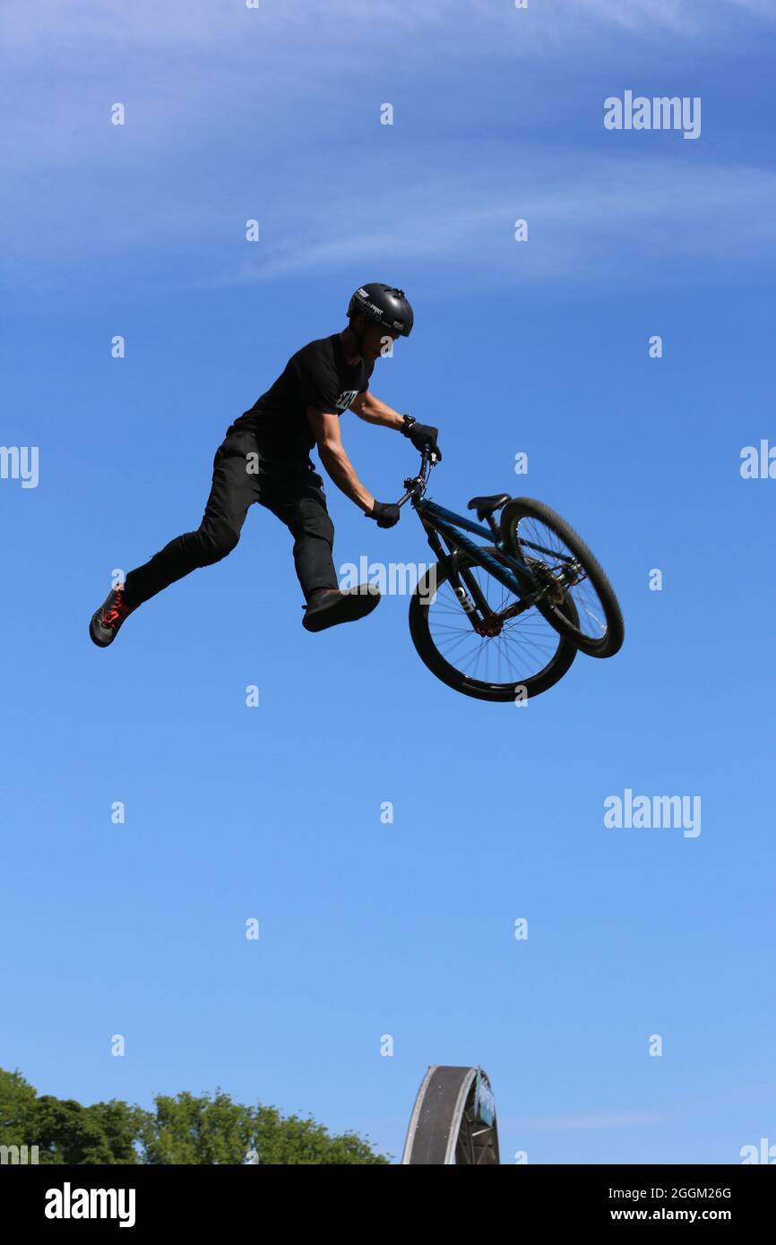 BMX or Mountain Biker high in the air doing a trick during a stunt show set against a mainly bright pale blue sky at the Isle of Man TT Stock Photo