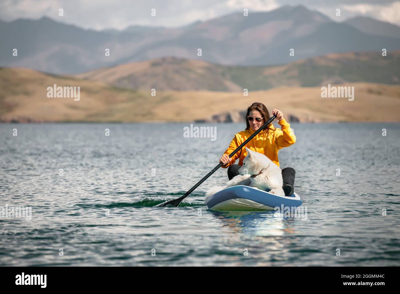 Girl walks on stand up paddle board at mountain lake with white siberian dog. Travel concept Stock Photo