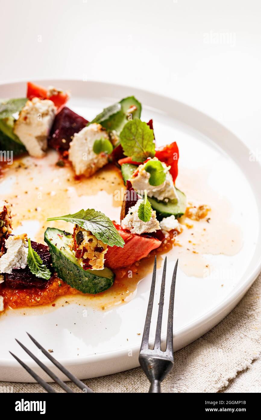 Close-up appetizing and fresh vegetable salad with beetroot, goat cheese, ripe tomato, cucumber, mustard leaves and spicy sauce. Delicious and healthy Stock Photo