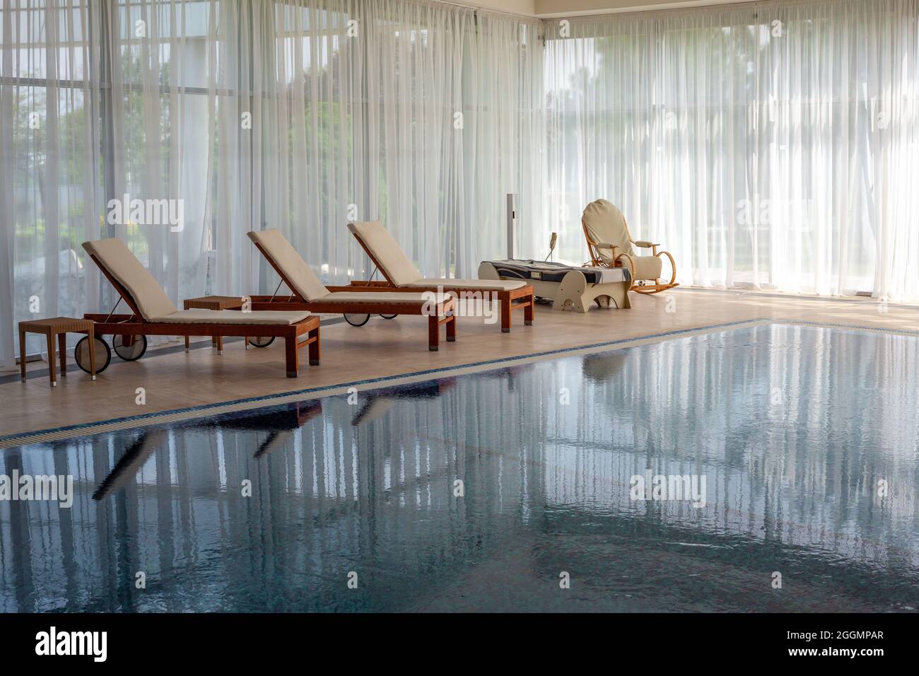 Relaxing area near indoor swimming pool with loungers, wicker rocking