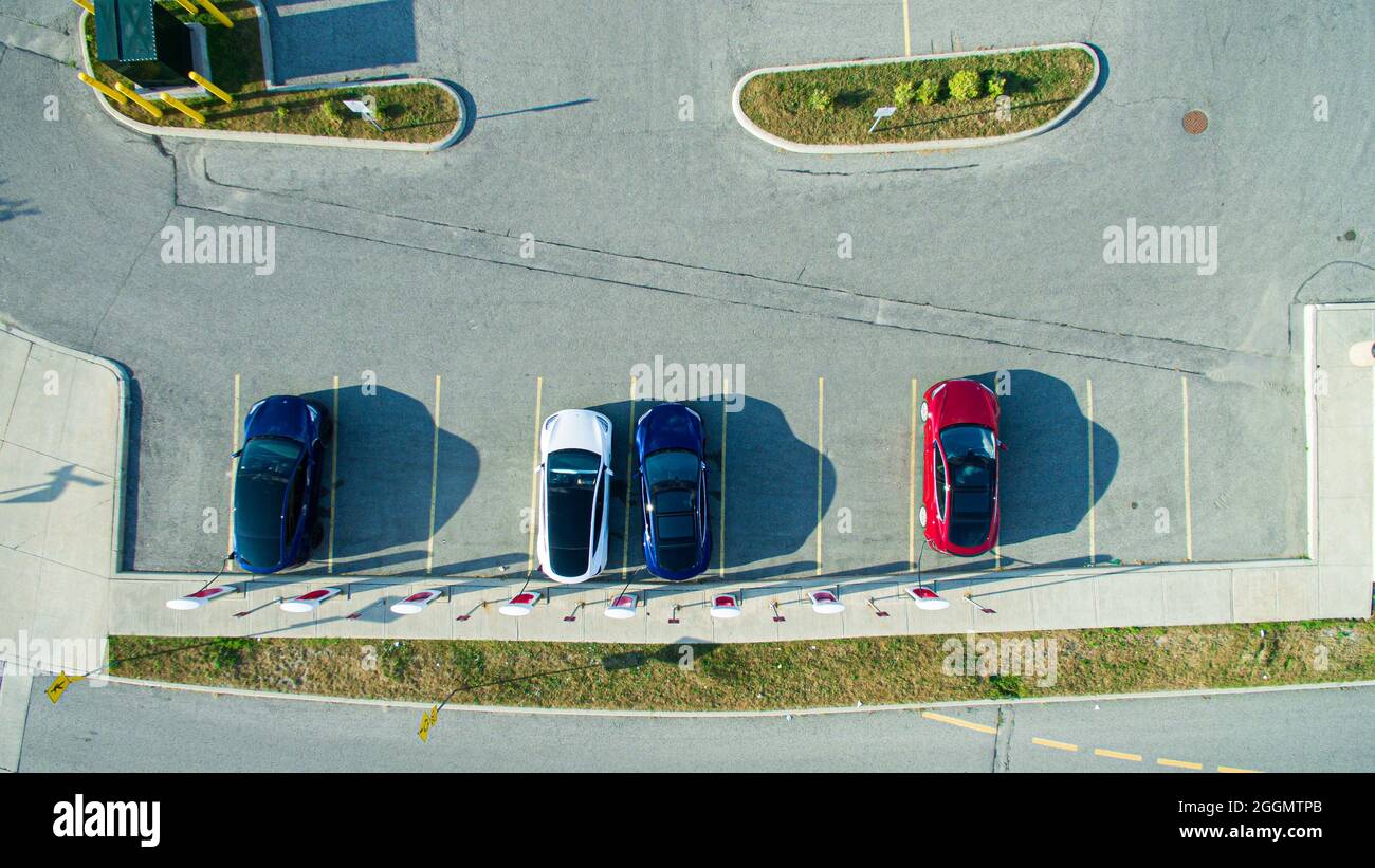 Overhead, drone view of Tesla vehicles charging at a Tesla Supercharger location on a sunny day. Stock Photo