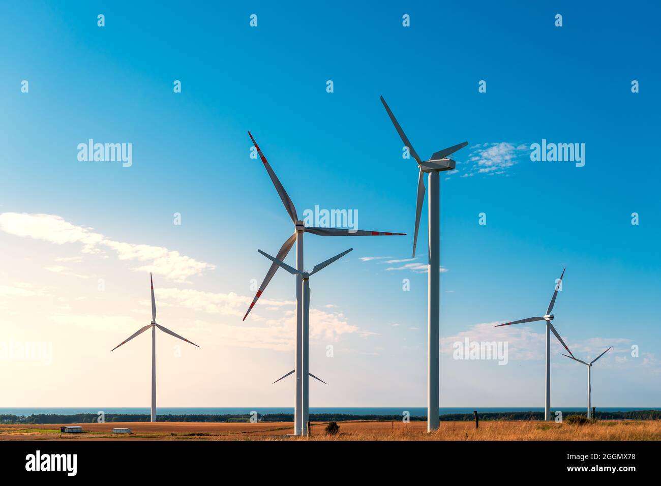 Windmills generating electricity located on a hill in the coastal area, the Baltic Sea in the background, wind farm against the blue sky, Poland Europ Stock Photo
