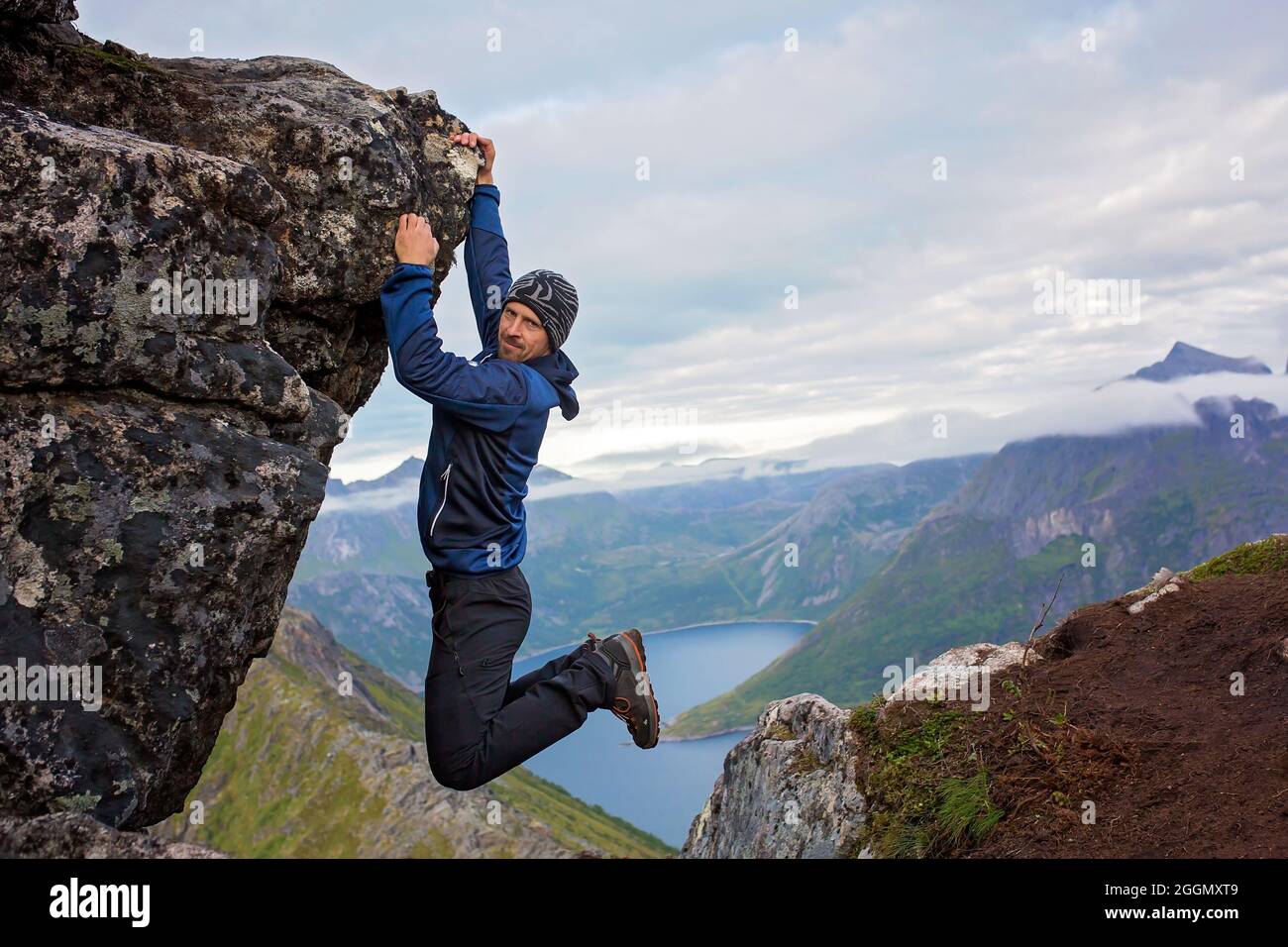 Happy child, hanging from a rock over Segla mountain on Senja island, North Norway. Amazing beautiful landscape and splendid nature in scandinavian co Stock Photo
