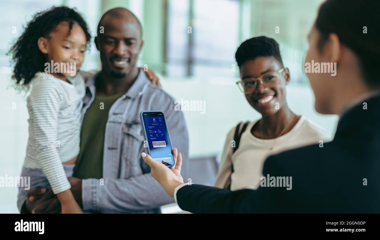 Airport staff looking at digital boarding pass on phone of tourist family at check-in counter. Airlines attendant checking boarding pass of passenger Stock Photo